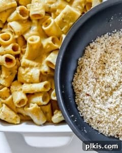 The panko breadcrumbs being sprinkled over the sauced pasta in the black baking dish, creating the crunchy topping.