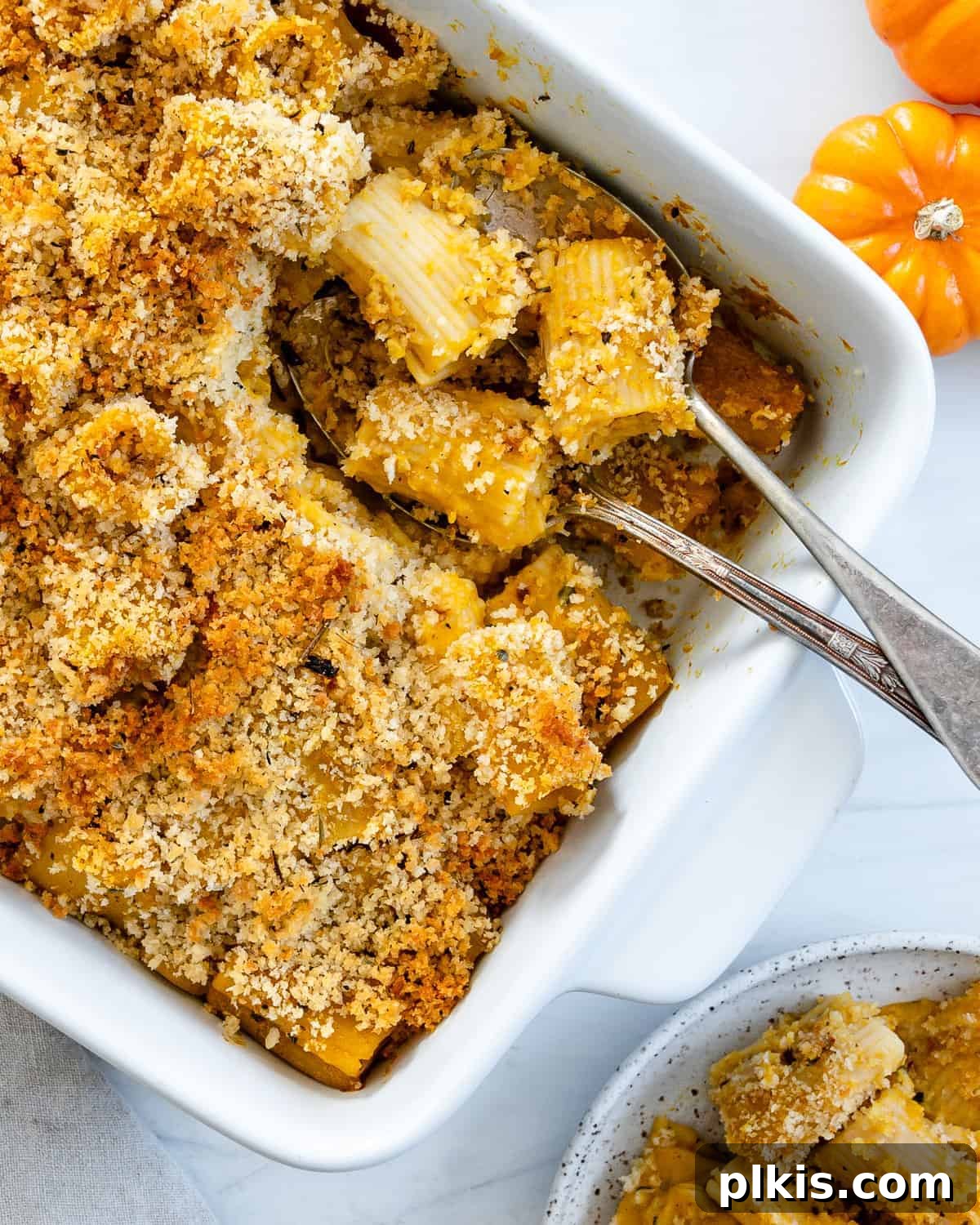 A perfectly baked vegan pumpkin pasta bake served in a white dish, with a fork and spoon resting in the dish, ready to be enjoyed.