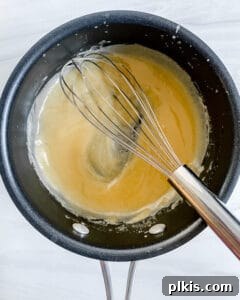 A whisk stirring the vegan butter and flour mixture in a black pan, forming a golden roux for the sauce.