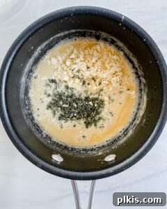 The process of adding vegetable broth slowly to the roux in a black pan, being whisked continuously to achieve a smooth sauce.