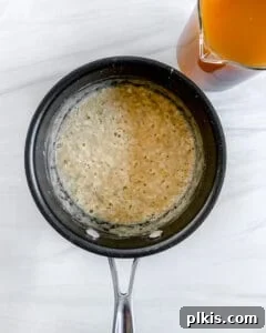 The simmering sauce in a black pan, thickening as it is whisked, showing its creamy texture.
