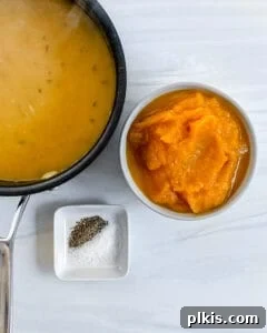Pumpkin puree being added to the thickened sauce in a black pan, next to other prepared ingredients, ready for whisking.