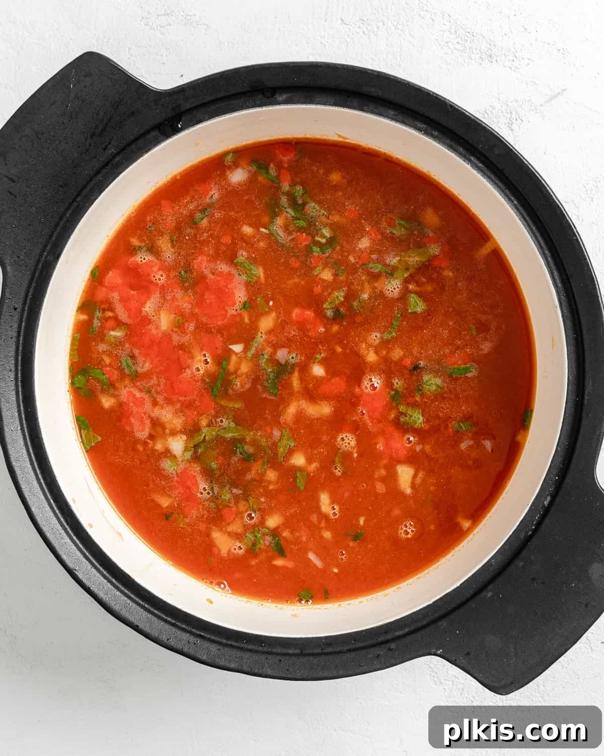 Turkish Embered Pepper Tomato Soup 12 Process shot of all soup ingredients - mint, tomatoes, pureed red peppers, and vegetable broth - simmering together in a large pot, creating a rich base for the Turkish Tomato, Bulgur, and Red Pepper Soup.