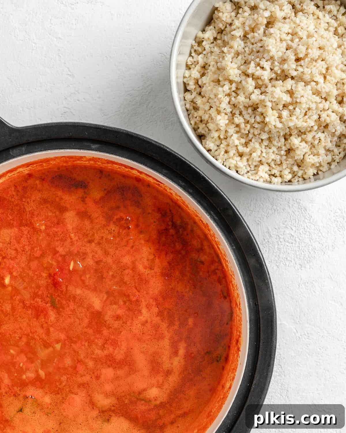 Turkish Embered Pepper Tomato Soup 13 Process shot featuring a bowl of soaked and drained bulgur wheat positioned next to a simmering pot of Turkish Tomato, Bulgur, and Red Pepper Soup base, ready for combination.