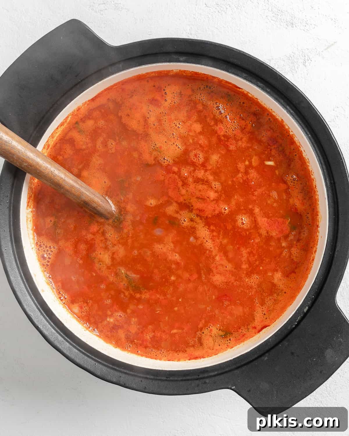 Turkish Embered Pepper Tomato Soup 14 Process shot showing the soaked bulgur wheat being added to the simmering pot of Turkish Tomato, Bulgur, and Red Pepper Soup, signifying the next step in thickening the soup.