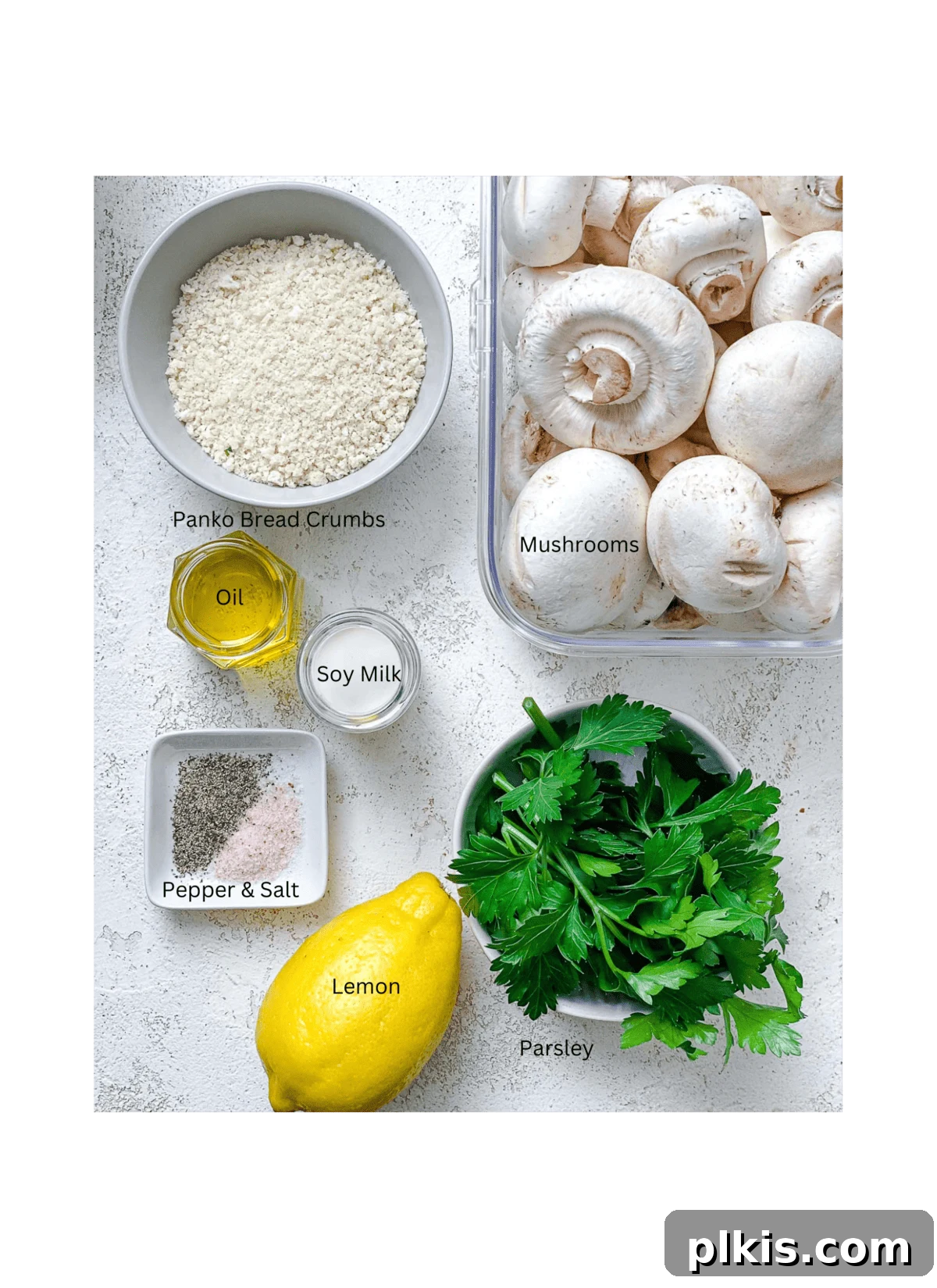 All the fresh ingredients for Easy Vegan Stuffed Mushrooms laid out neatly on a white surface: mushrooms, panko breadcrumbs, plant-based milk, lemon, fresh parsley, olive oil, salt, and pepper.