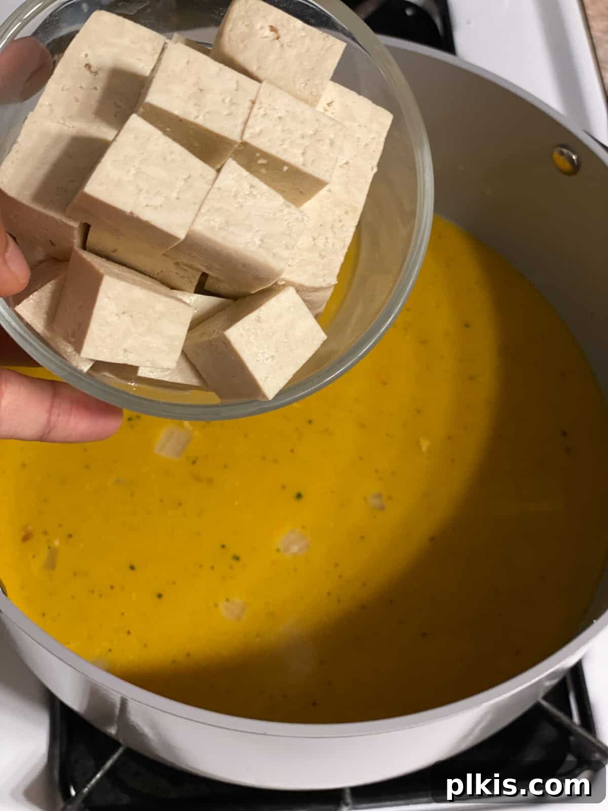 Golden Pumpkin Curry 5 A process shot demonstrating cubed tofu being gently added to the pot, ready to be incorporated into the curry.
