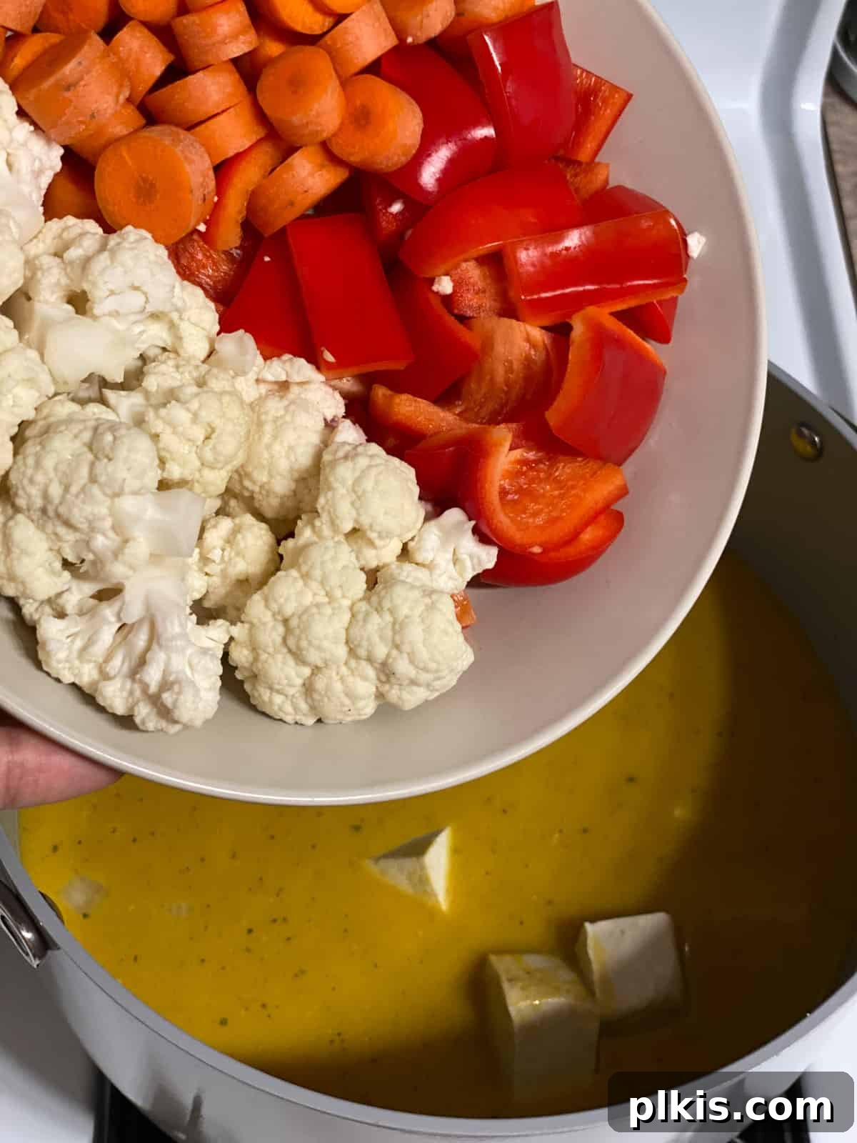 Golden Pumpkin Curry 6 A close-up process shot of various colorful vegetables being added to the simmering pumpkin curry, enhancing its visual appeal and nutrition.