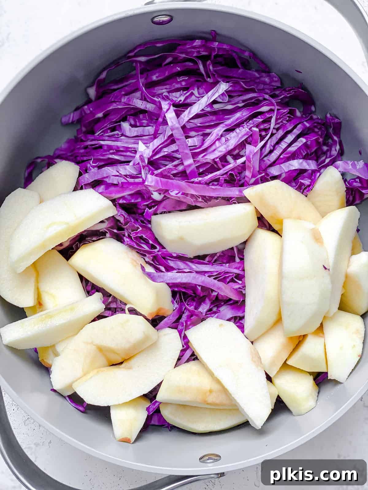Braised German Red Cabbage with Apples and Warm Spices 4 Process shot showing sliced apples being added to a large pot with shredded red cabbage.