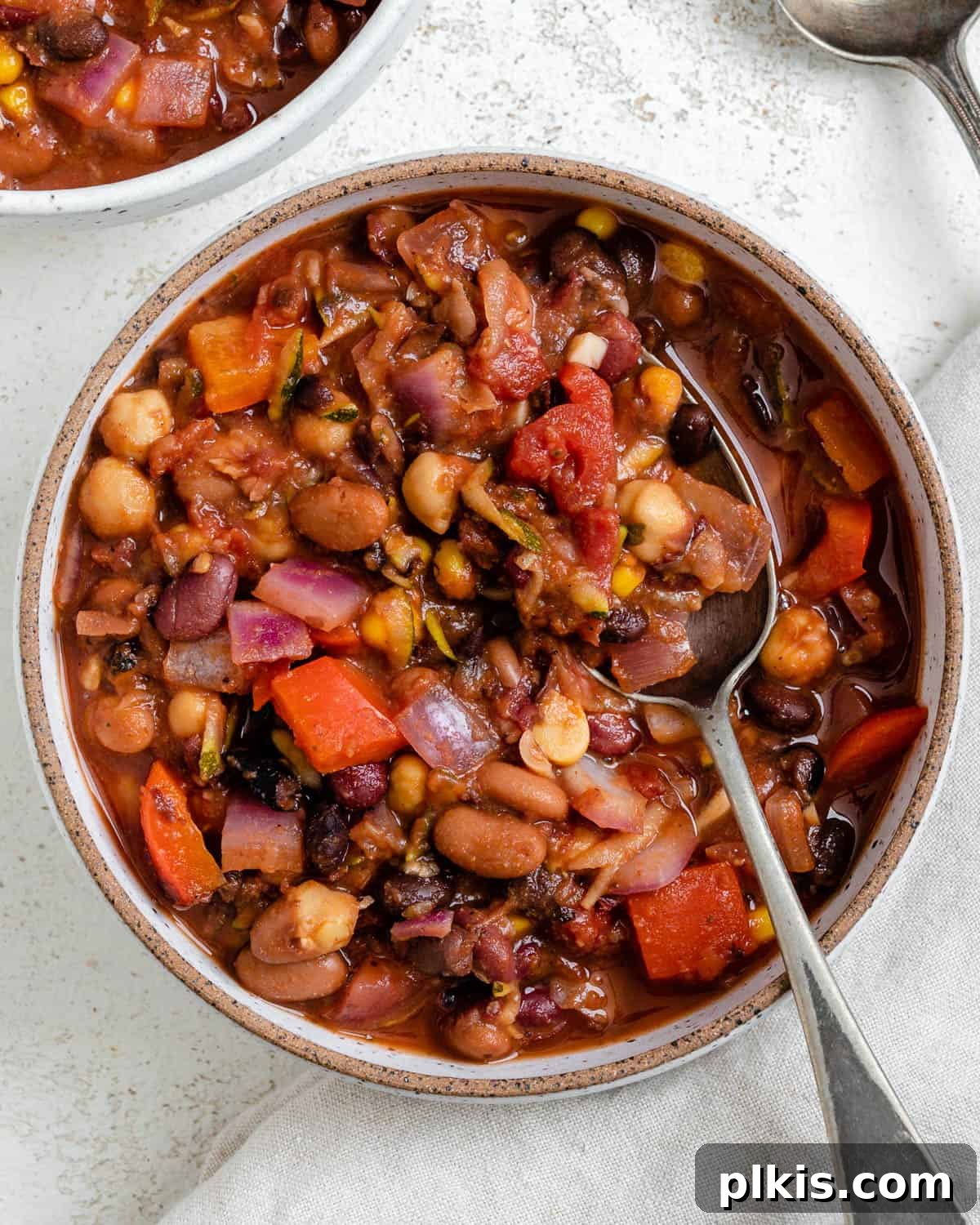 The Ultimate Vegan Bean Chili stovetop Slow Cooker Instant Pot 2 Completed Vegan Bean Chili plated in a bowl against a light background, garnished with fresh herbs and a slice of lime.