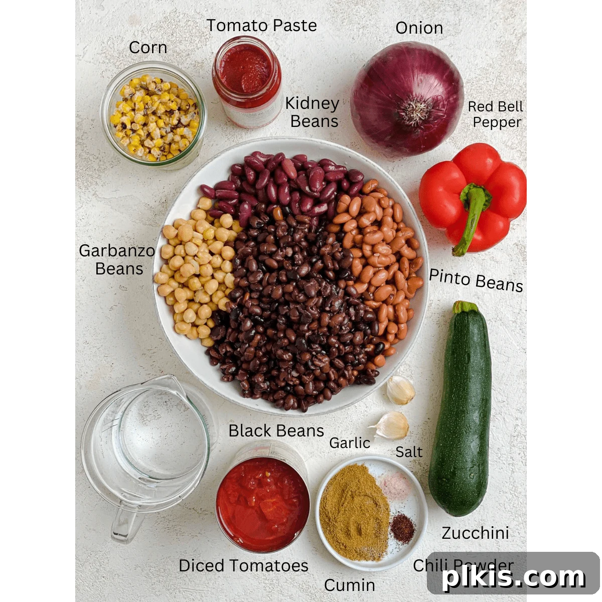 The Ultimate Vegan Bean Chili stovetop Slow Cooker Instant Pot 3 A selection of fresh and canned ingredients for Crockpot Four Bean Chili, including various beans, vegetables, and spices, arranged neatly on a white surface.