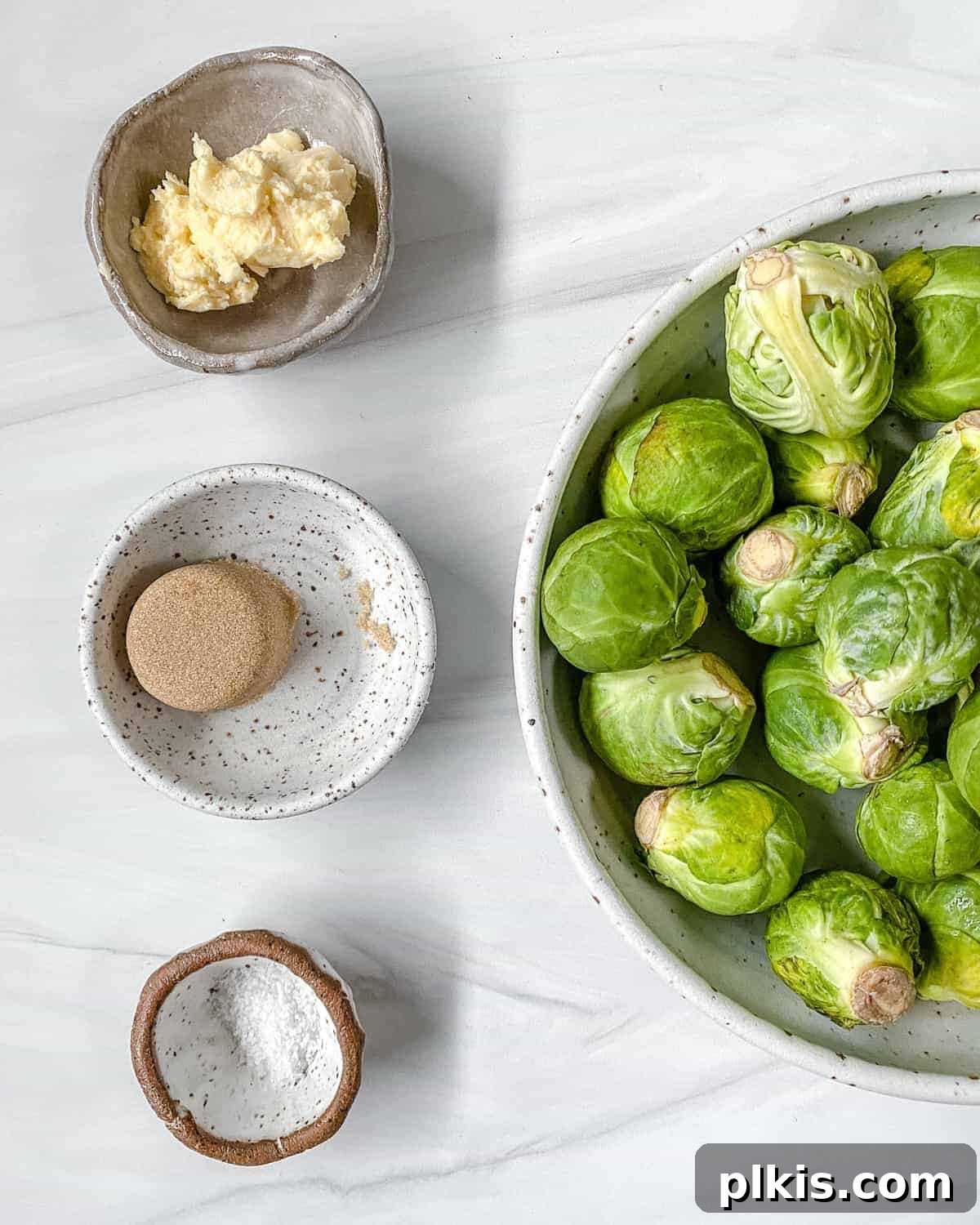All the simple ingredients for Sweet and Salty Brussels Sprouts laid out on a white surface.