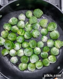 Halved Brussels sprouts being added to the pan, cut-side down, into the melted glaze.