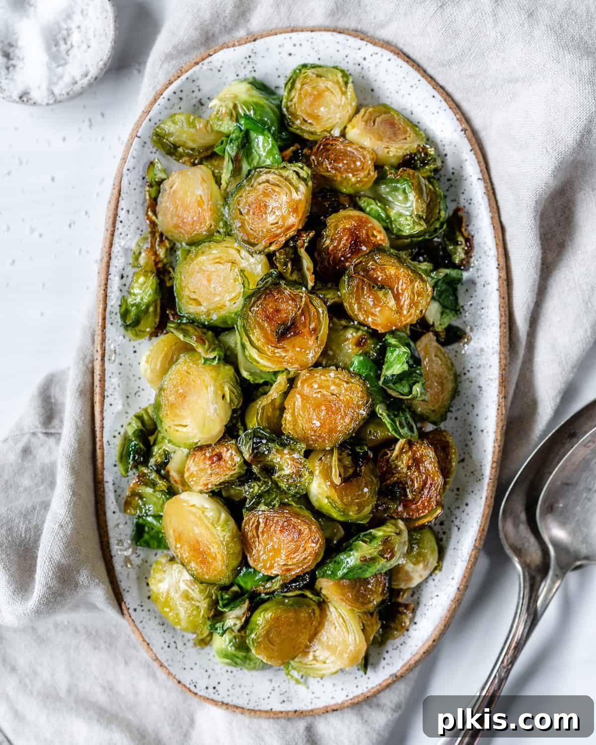 A generous serving of completed Sweet and Salty Brussels Sprouts in a white bowl, against a bright white background, ready to be enjoyed.