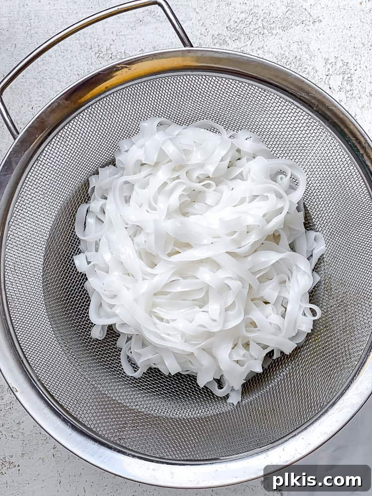 Process shot showing vermicelli noodles being strained under cold water in a colander.