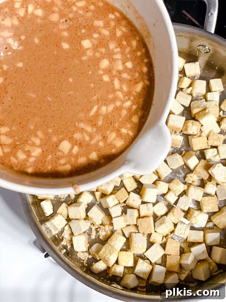Process shot showing the peanut sauce being added to pan with golden-brown tofu cubes.