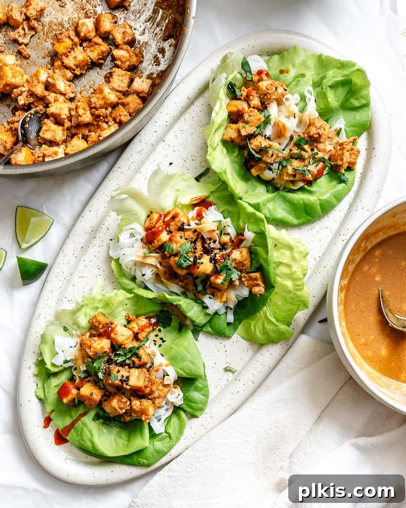 Close-up of completed Tofu Lettuce Wraps with Peanut Sauce on a decorative platter, showing texture and garnishes.