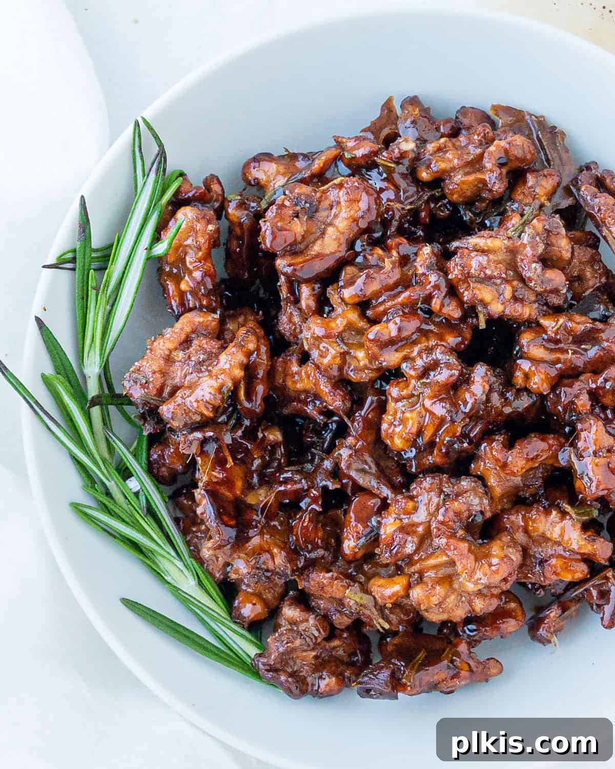 Rosemary Glazed Walnuts 3 Completed sweet rosemary walnuts plated on a white plate against a white surface, showcasing their delicious glaze and perfect texture.