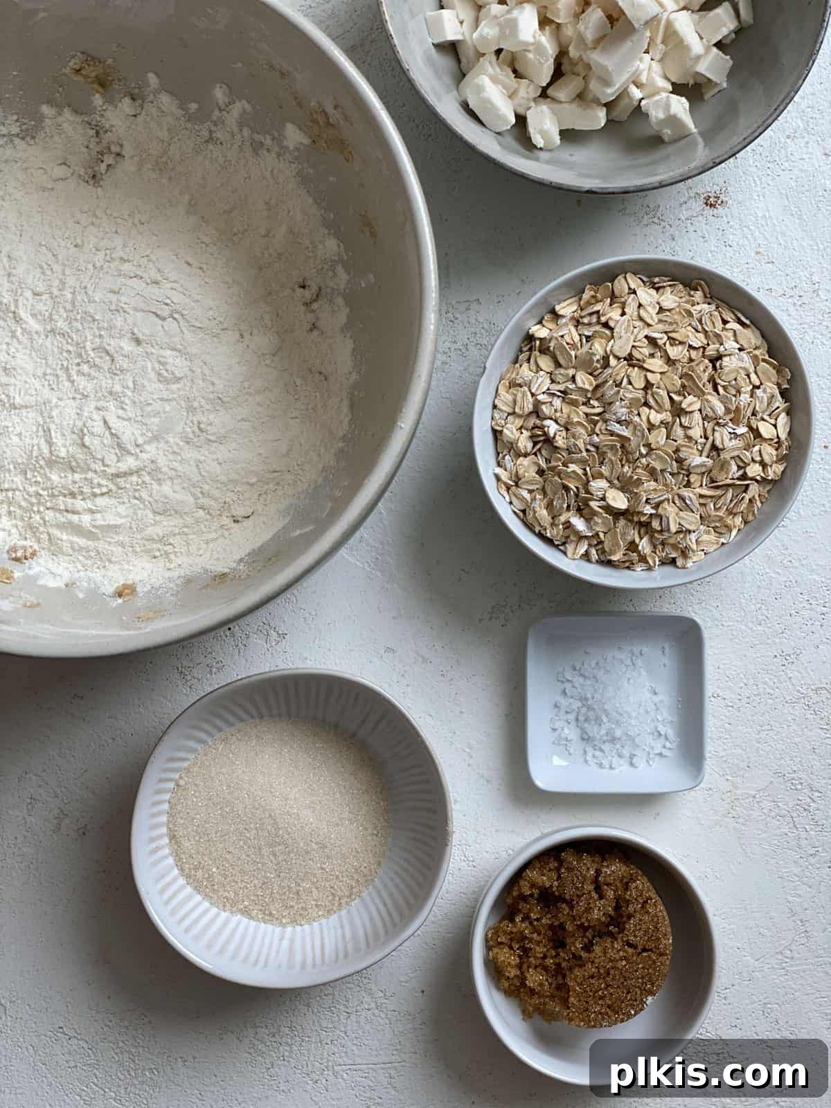 Autumn Apple Cranberry Delight 4 Ingredients for Apple Cranberry Crisp topping measured out on a white surface, showing flour, brown sugar, salt, and cold vegan butter cubes, ready for mixing.
