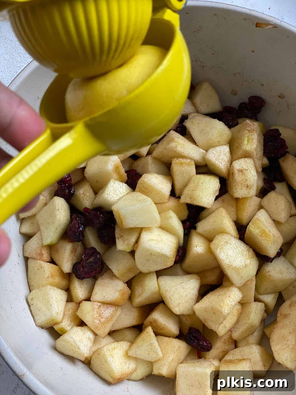 Autumn Apple Cranberry Delight 8 Process shot of fresh lemon being juiced directly into a bowl of chopped apples and other filling ingredients, to prevent browning and add flavor.