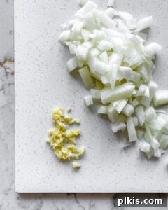 Close-up of chopped garlic and onion on a white cutting board, prepped for cooking.