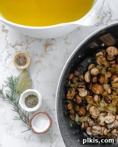 Various aromatics and herbs measured out in individual bowls, next to a pot of ingredients on a white marble background.