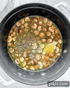 Velvet Mushroom Elixir 9 All the ingredients for mushroom orzo soup simmering together in a black pan, creating a rich broth.