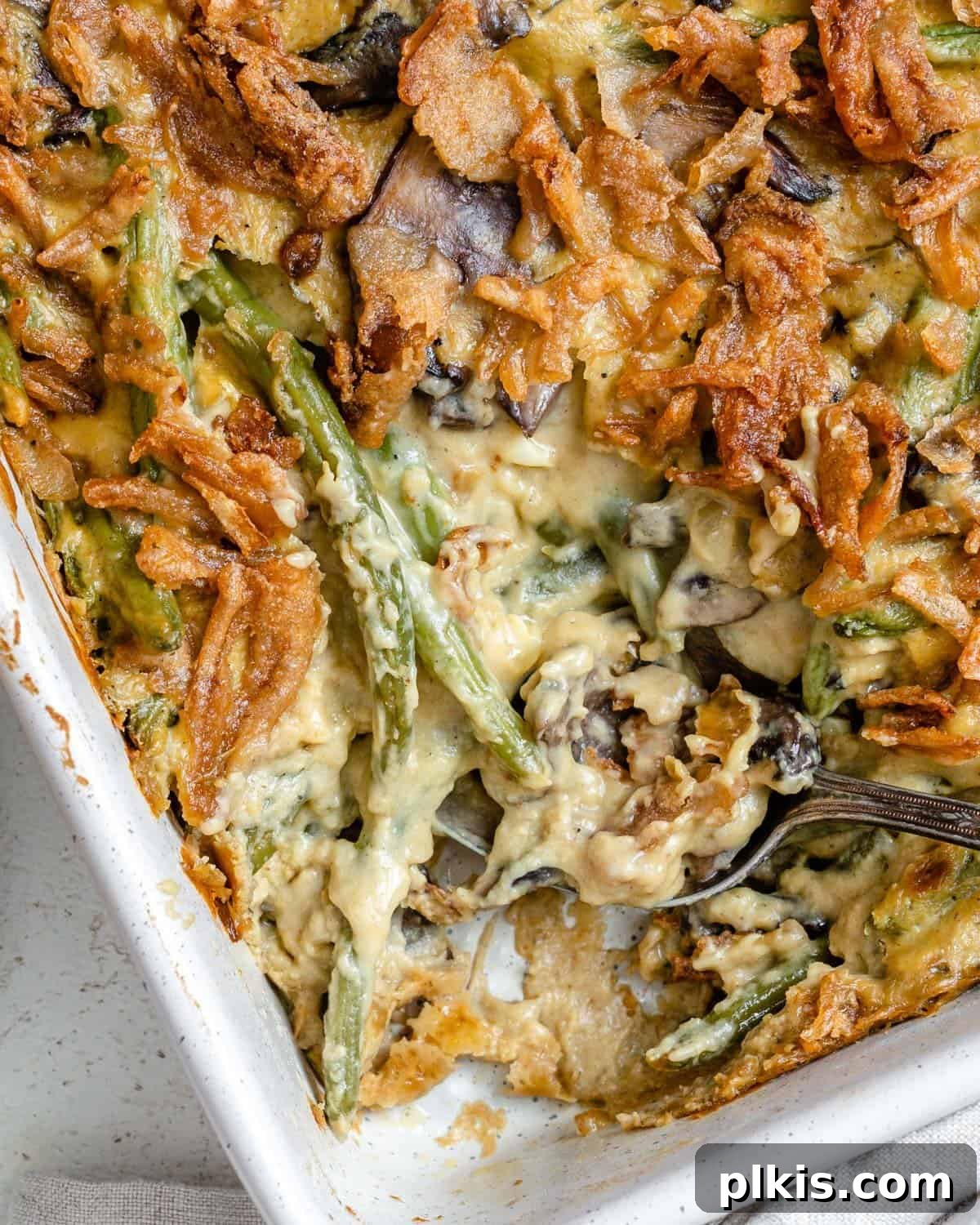 Plant-Powered Green Bean Casserole 2 Beautifully baked Dairy-Free Green Bean Casserole in a white baking dish, topped with golden crispy onions.