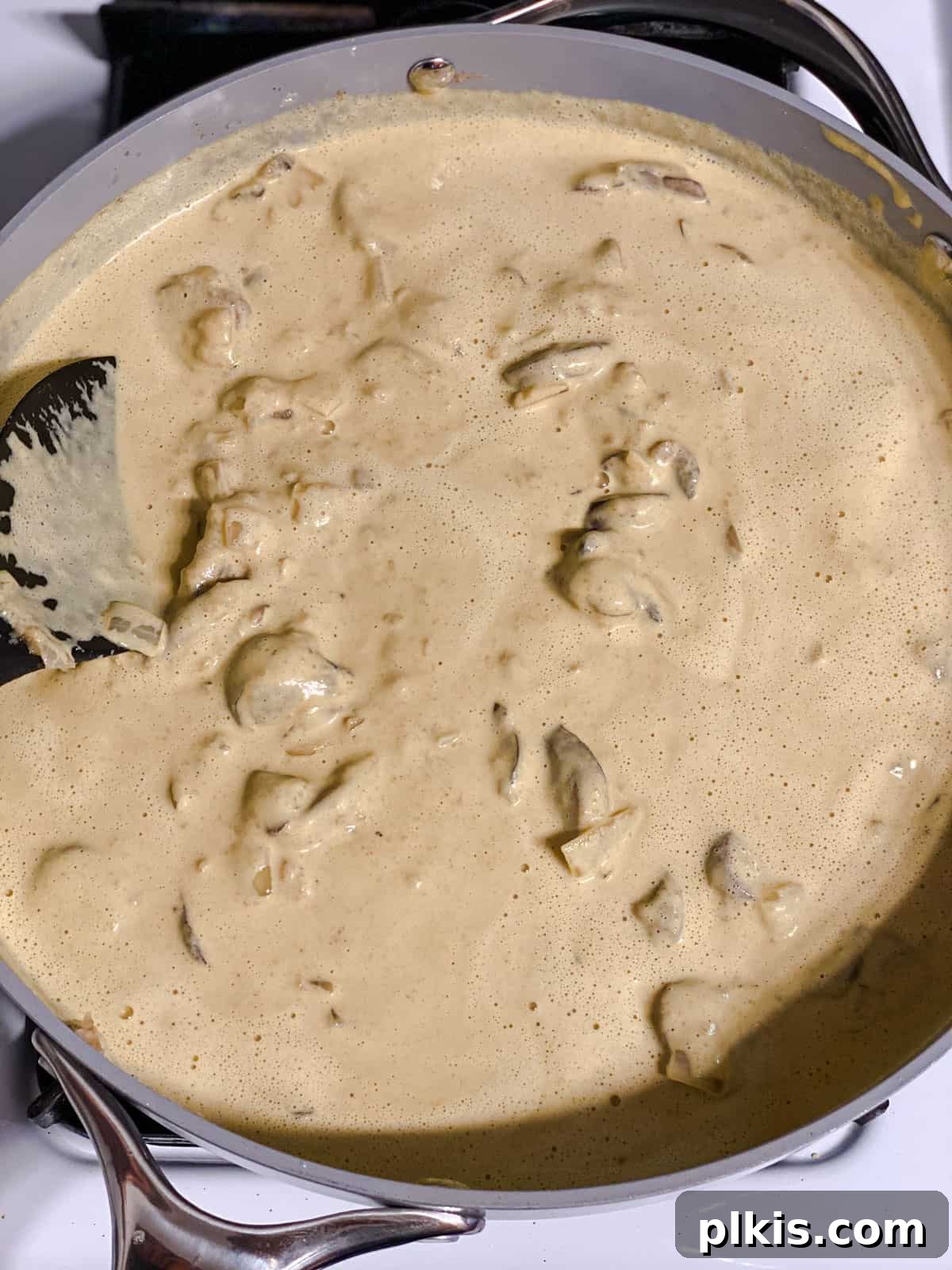 Plant-Powered Green Bean Casserole 6 Process shot of flour, cashew cream, and sautéed vegetables being whisked together in a pan to create a thickened sauce.