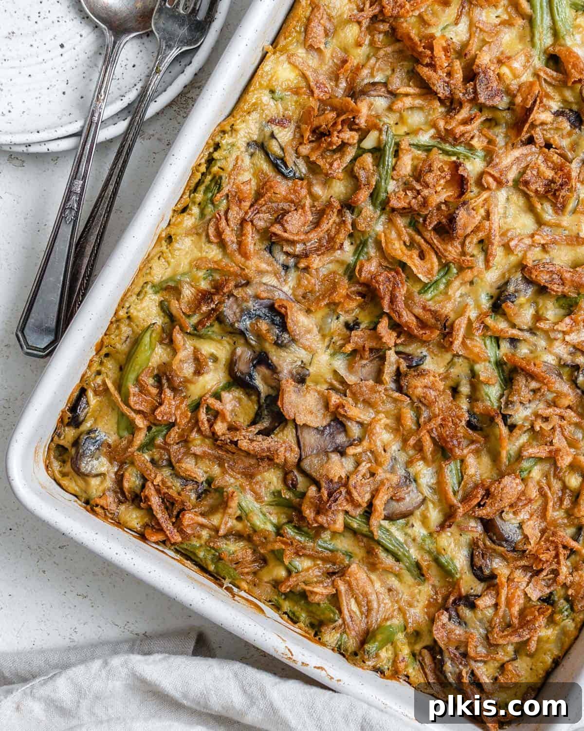 Plant-Powered Green Bean Casserole 8 Close-up shot of the super creamy Dairy-Free Green Bean Casserole in a white baking dish, showing the perfectly browned crispy onion topping and tender green beans peeking through the rich sauce.
