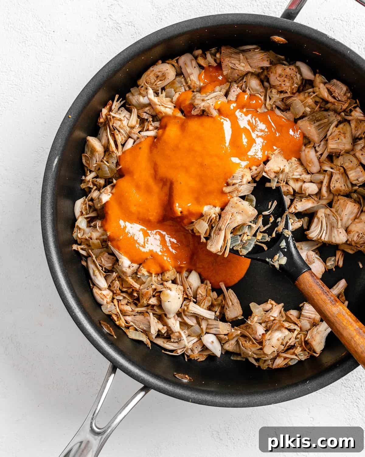 Smoky Vegan Jackfruit BBQ 12 process of adding bbq sauce to pan of jackfruit against white background