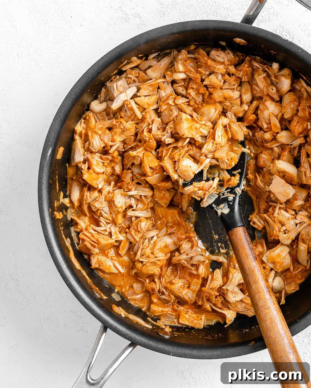 Smoky Vegan Jackfruit BBQ 13 process of mixing bbq sauce to pan of jackfruit against white background