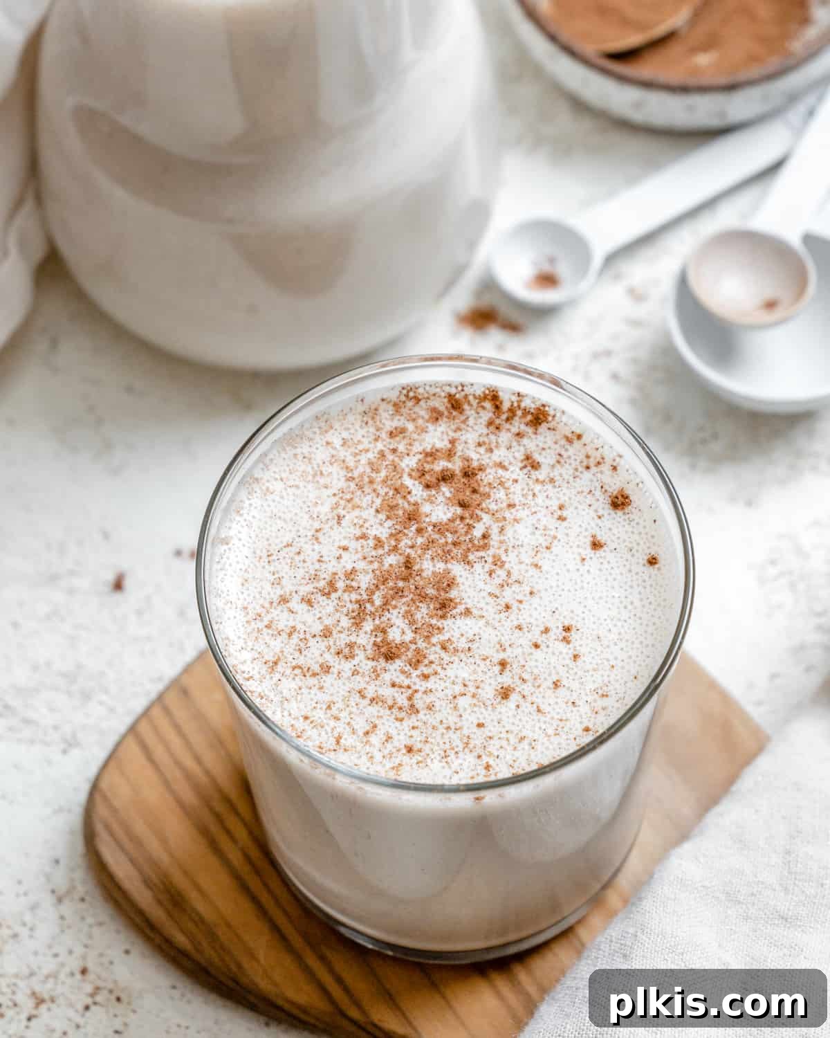 Effortless Dairy-Free Eggnog 2 A festive glass of creamy vegan eggnog, garnished with cinnamon, on a rustic brown and white surface, ready for the holidays.