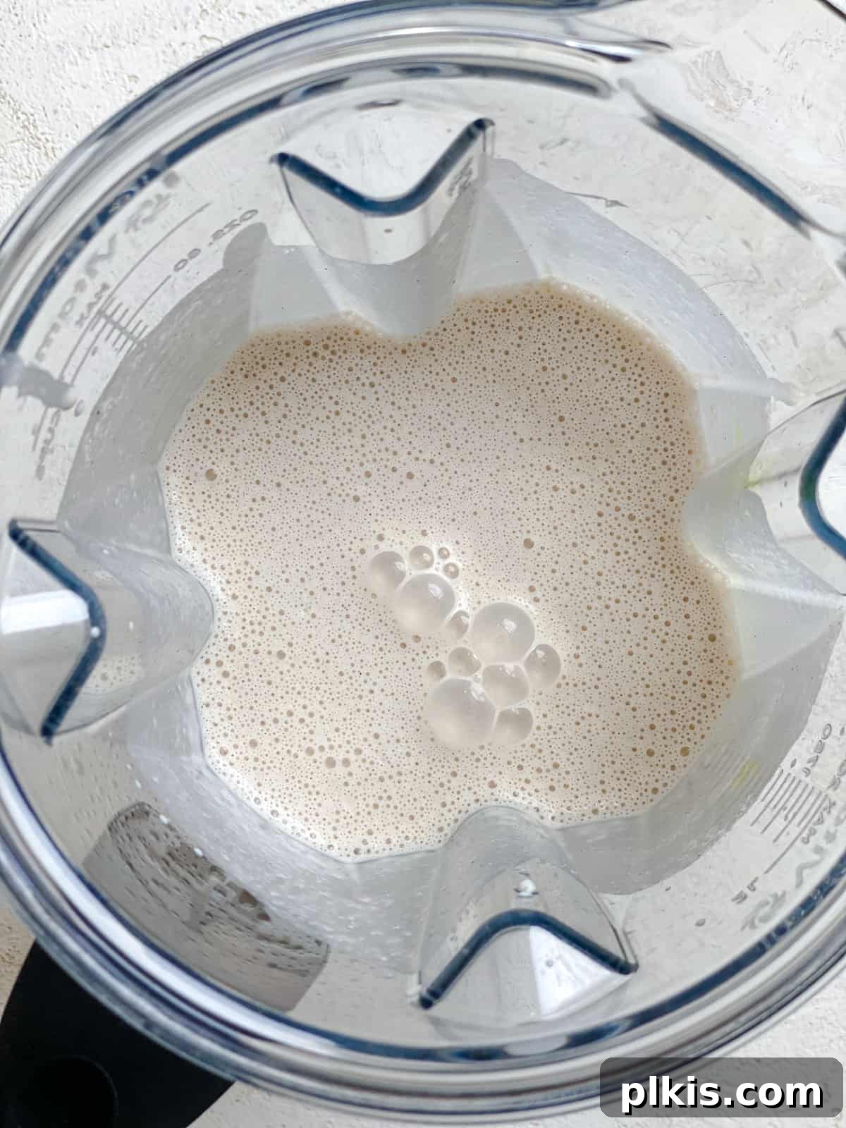 Effortless Dairy-Free Eggnog 5 A process shot demonstrating a smooth stream of plant-based milk being poured into a blender filled with eggnog ingredients, ensuring a creamy consistency.
