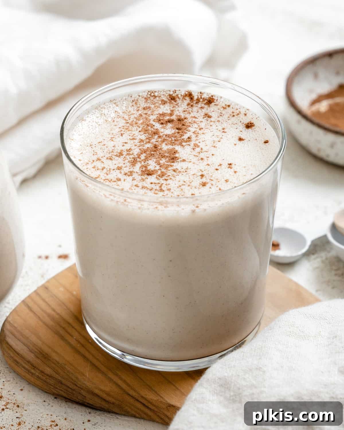 Effortless Dairy-Free Eggnog 6 A beautifully garnished glass of Easy Vegan Eggnog sits on a warm brown and white surface, inviting holiday cheer, ready for serving.