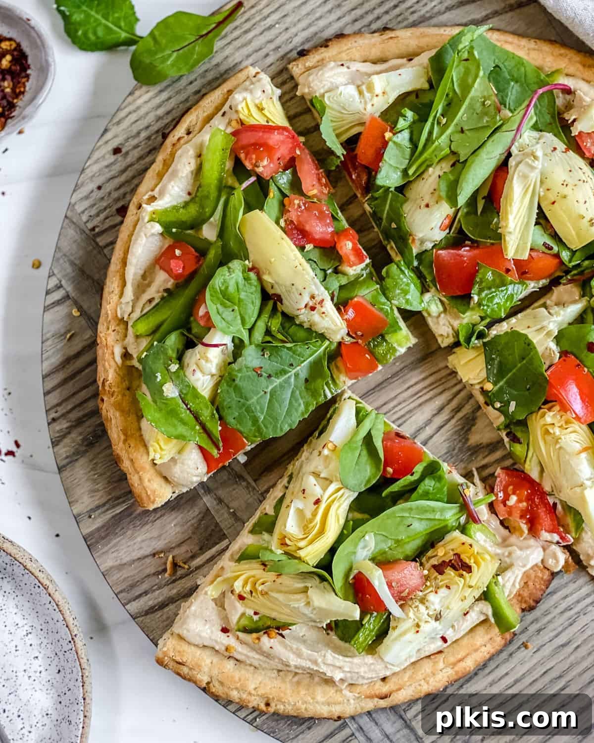 Mediterranean Hummus Pizza: Dairy-Free and Your Way 2 Completed hummus pizza sliced on a gray surface, garnished with fresh herbs.