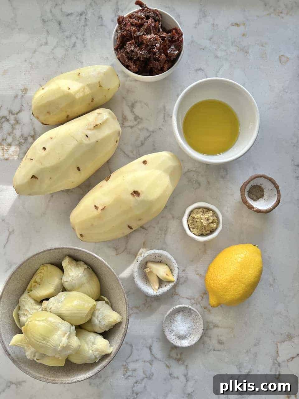 Zesty Artichoke and Potato Salad 3 Ingredients for Artichoke Potato Salad with Lemon Dressing measured out against a white surface, including potatoes, artichokes, lemons, and sun-dried tomatoes.