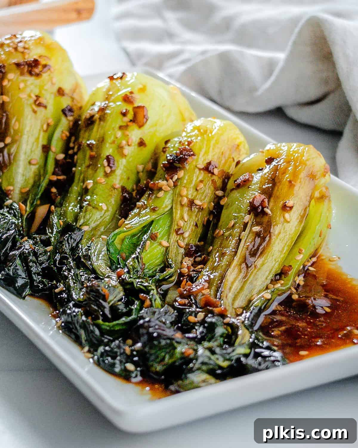 Garlic Soy Glazed Baby Bok Choy 2 A beautifully presented plate of stir-fried baby bok choy with soy sauce and garlic, garnished with sesame seeds, on a white serving tray, ready to be enjoyed.