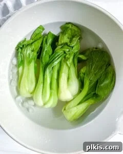 Garlic Soy Glazed Baby Bok Choy 4 Freshly blanched baby bok choy cooling in a pristine white bowl filled with ice water, preserving its vibrant green color.