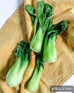 Garlic Soy Glazed Baby Bok Choy 5 Cleaned baby bok choy stalks and leaves gently drying on a light tan cloth, ensuring all excess moisture is removed before cooking.