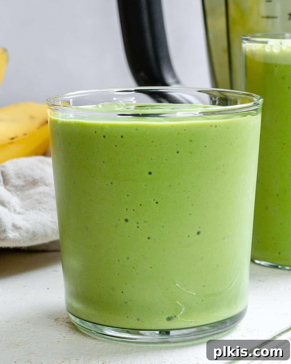 Creamy Kale Banana Bliss 5 Two glasses of completed Banana Kale Smoothie with a sprinkle of chia seeds, placed on a light wooden surface with fresh banana and kale in the background.