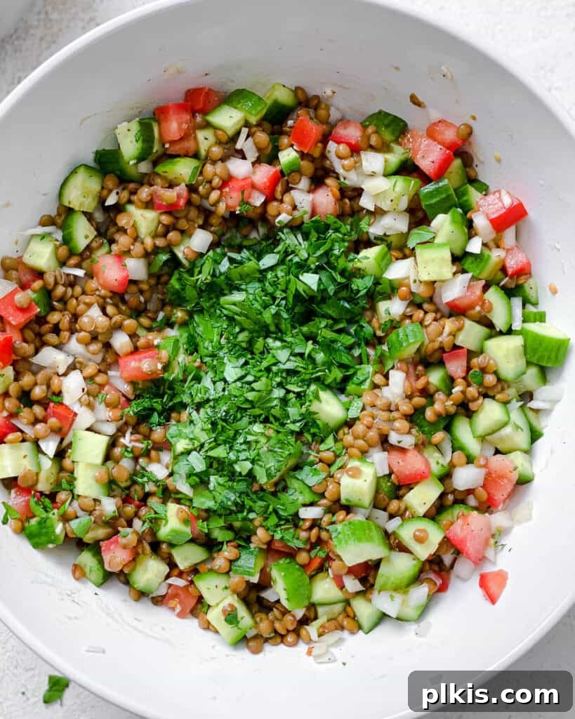 Fresh and Flavorful Lentil Tabbouleh 12 Process shot of adding fresh herbs to the bowl of lentils and vegetables.