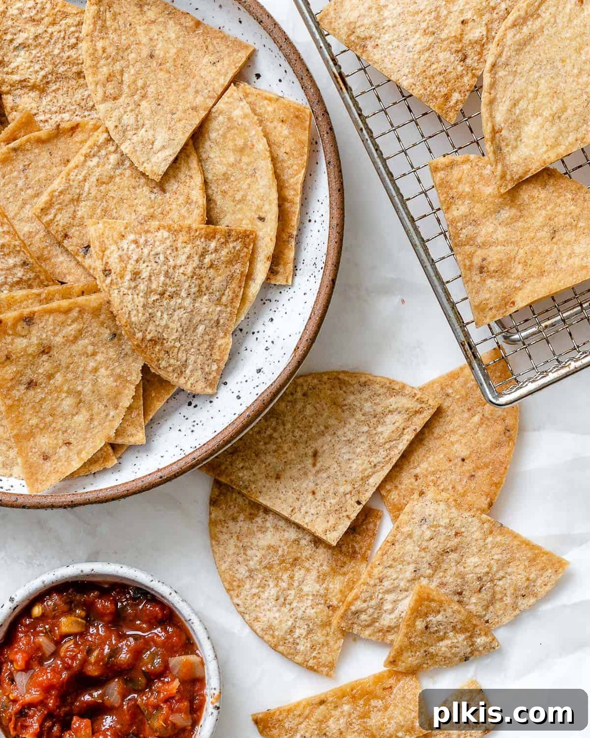 The Crispiest Air Fryer Tortilla Chips 2 completed Air Fryer Tortilla Chips plated alongside chips against a white surface with salsa on the side