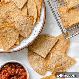 completed Air Fryer Tortilla Chips plated alongside chips against a white surface with salsa on the side