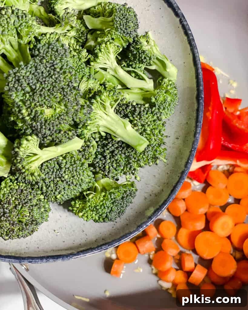 Broccoli florets being added to the pan, completing the initial batch of vegetables for stir-frying.