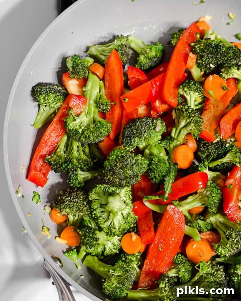 Various vegetables actively cooking in the pan, stirring to ensure even heat distribution and crisp texture.