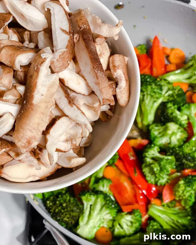 Sliced mushrooms being added to the stir-frying vegetables in the pan, adding an earthy depth to the dish.