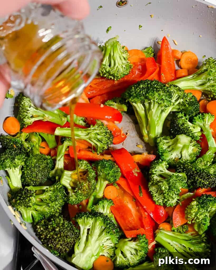 A drizzle of sesame oil being added to the cooking vegetables in the pan, enhancing their flavor and aroma.