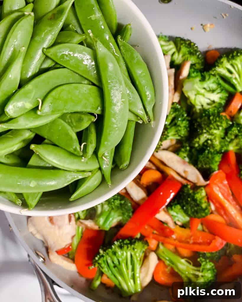 Sugar snap peas being added to the stir-fry, contributing a fresh, crisp element to the vibrant vegetable mix.