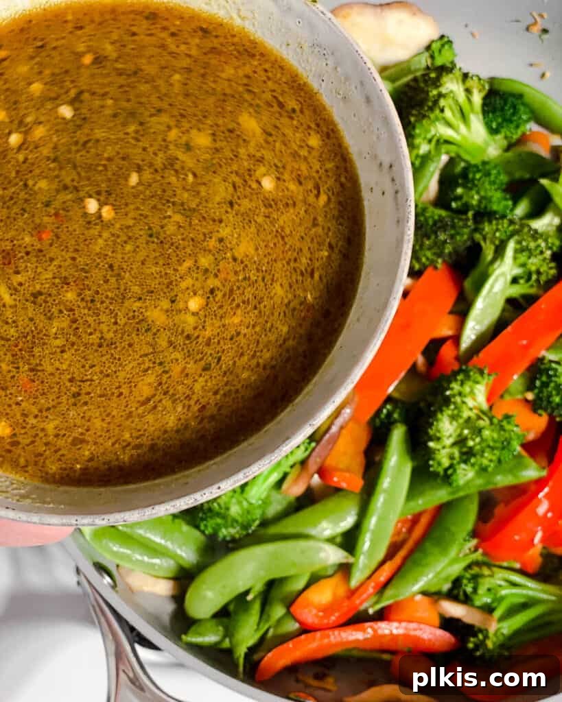 The prepared stir-fry sauce being poured over the cooked vegetables in the pan, ready to thicken and coat.